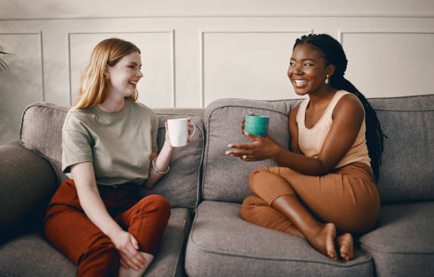 Two women smiling and chatting over drinks on a sofa